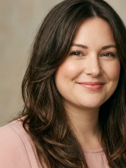 Woman with long layered brown hair parted off-center framing her face in soft studio light
