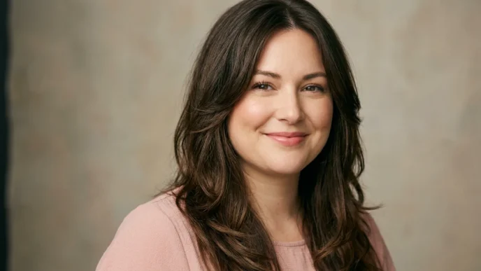 Woman with long layered brown hair parted off-center framing her face in soft studio light