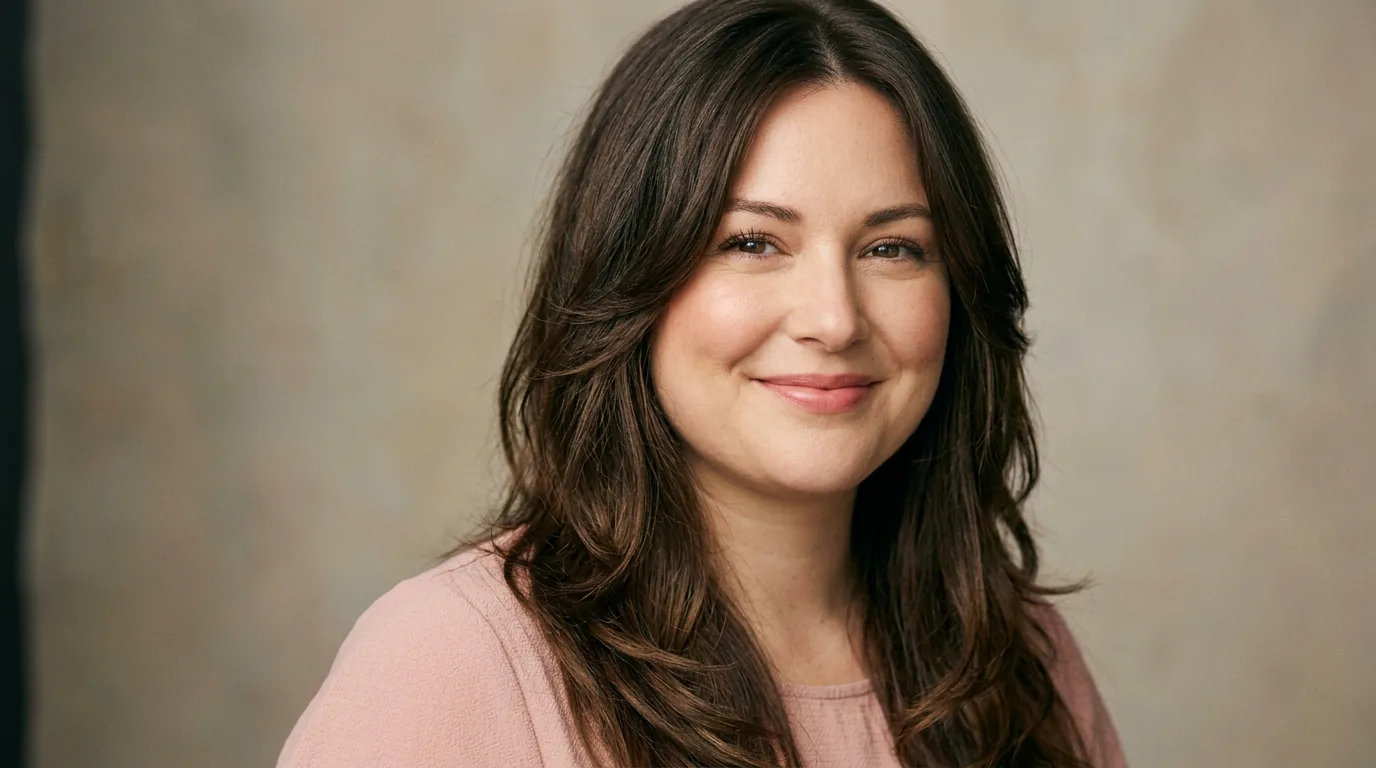 Woman with long layered brown hair parted off-center framing her face in soft studio light