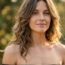 Woman with shoulder length layered wavy hair falling over bare shoulders in golden light
